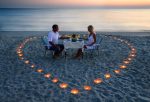 A young lovers couple share a romantic dinner with candles heart on the sea sand beach